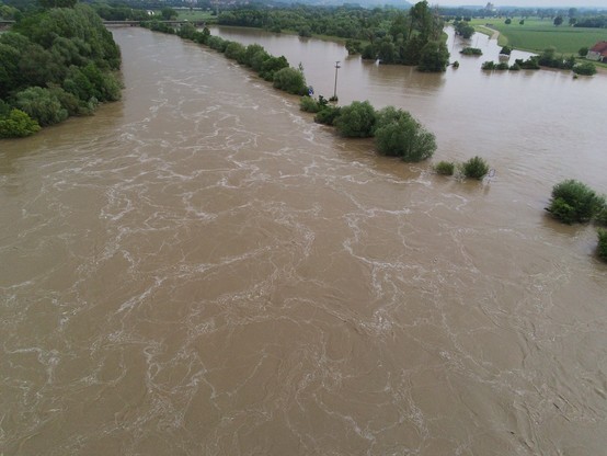 Aerial view of a flooded river overflowing its banks near Donauwoerth, with trees and vegetation partially submerged in the water.