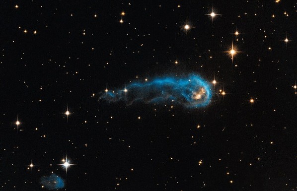Das Weltraum-Foto zeigt das schwarze Weltall mit weißlich bis gelblich leuchtenden Sternen von etwa einem bis fünf Millimetern Größe. In der Bildmitte eine längliche, außen blau leuchtende Wolke. - Foto: NASA, ESA, and the Hubble Heritage Team (STScI/AURA), unter Lizenz CC BY 2.0 (siehe t1p.de/ccby20) via Wikimedia Commons
