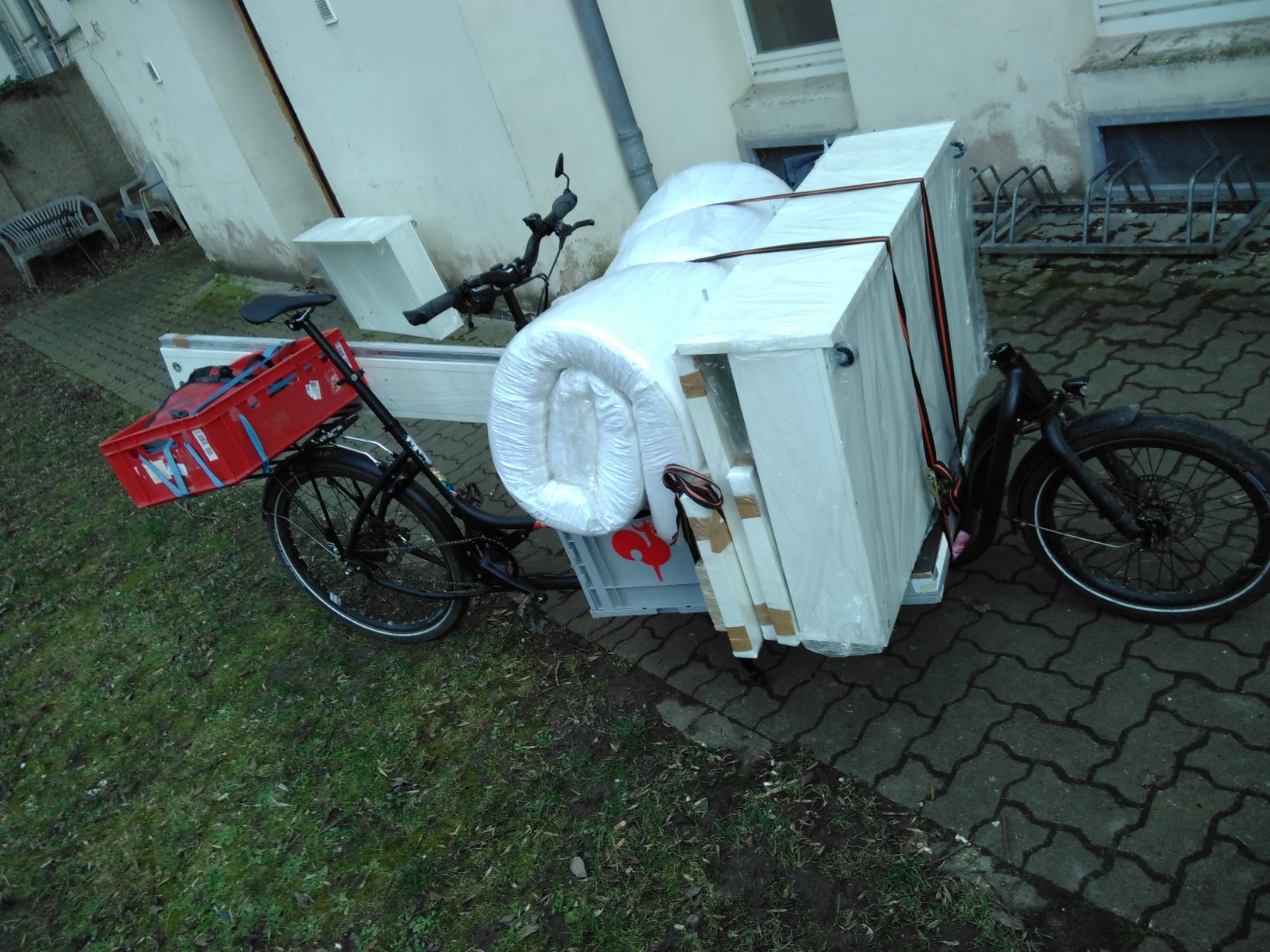 Ein Bett auf dem Lastenrad: Matratze und Betkästen auf der Ladenfläche, Rahmen seitlich gelascht.