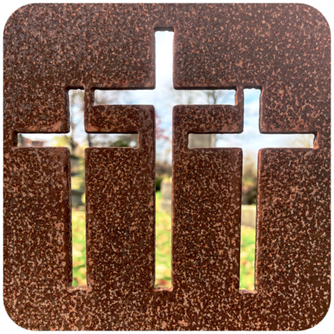 rostige Stahlplatte mit drei eingefrästen Kreuzen, hindurch erkenn kann man Rasen und Grabstellen